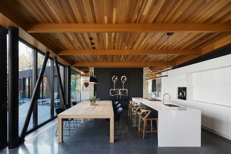 نمای داخلی آشپزخانه مدرن با کابینت های سفید و میز چوبی بلند