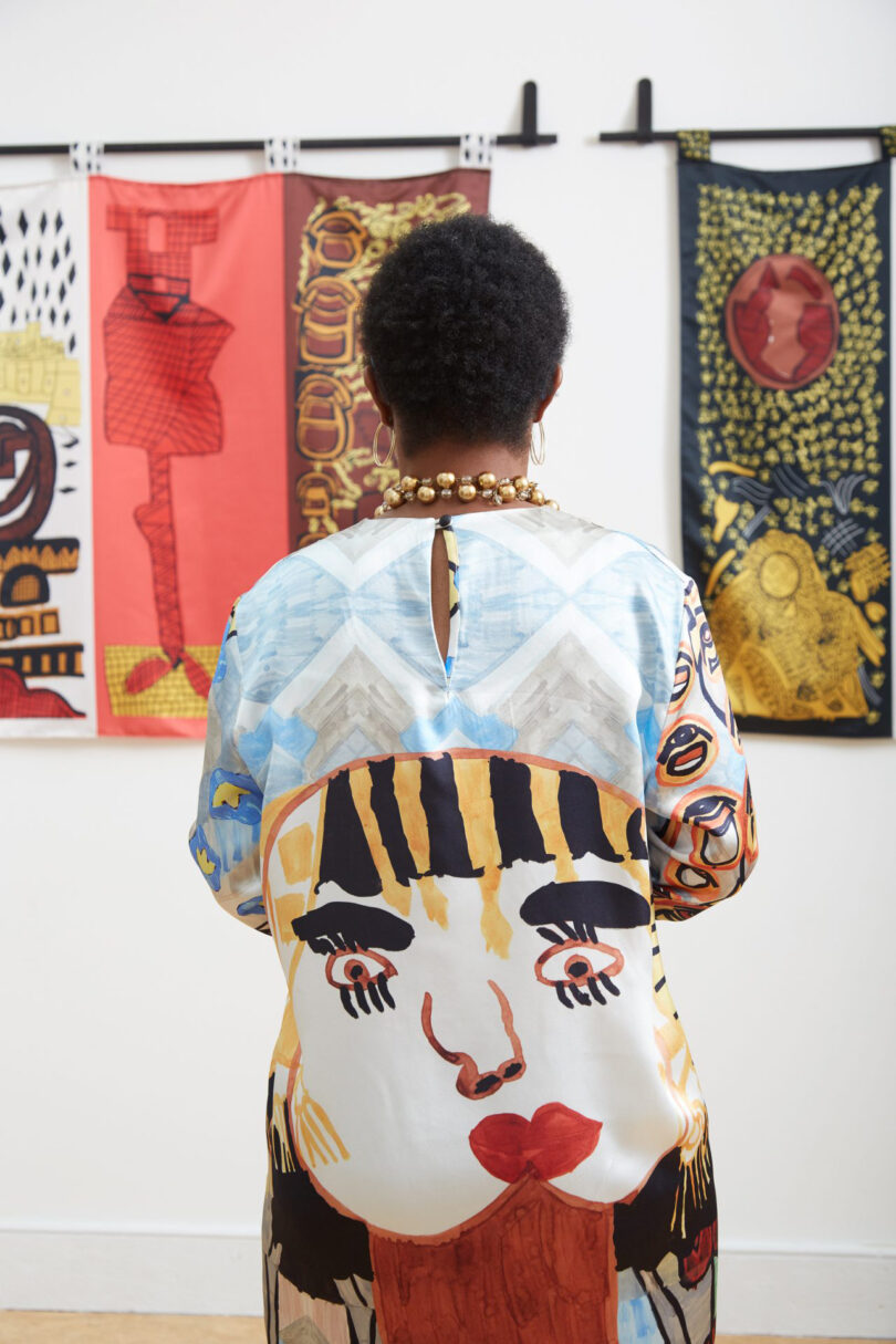 a woman with short black hair looks at a wall of tapestries