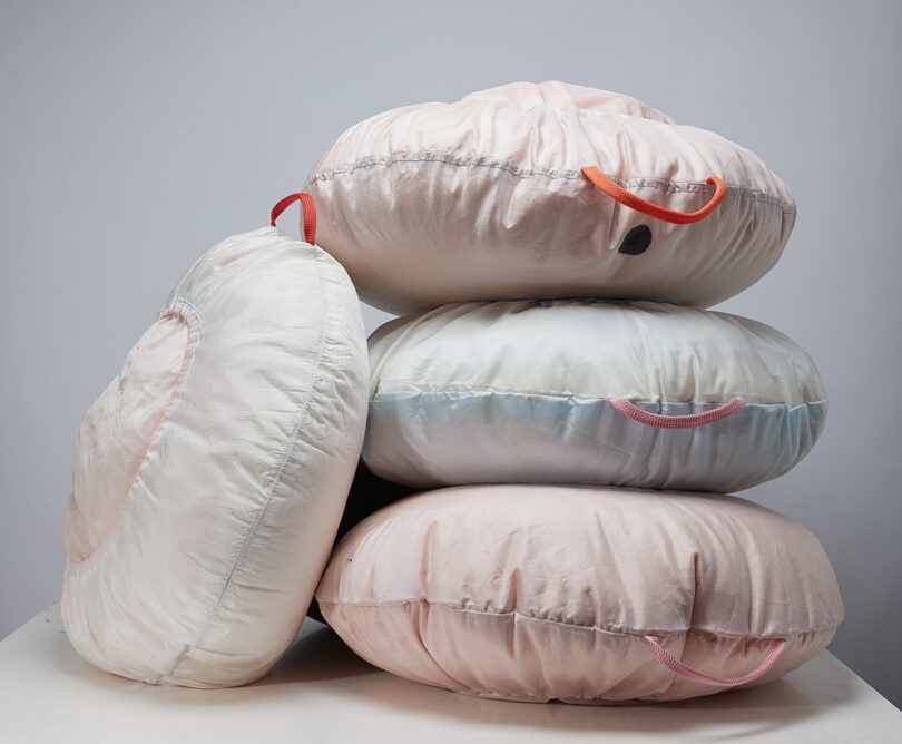Stack of round pastel colored pillows made from recycled car air bags with orange handles.