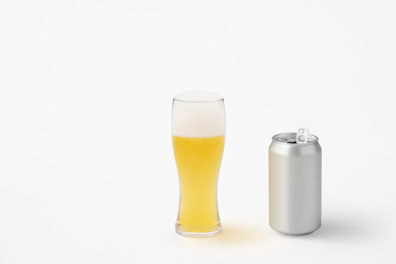 chrome beer can sitting next to glass filled with beer