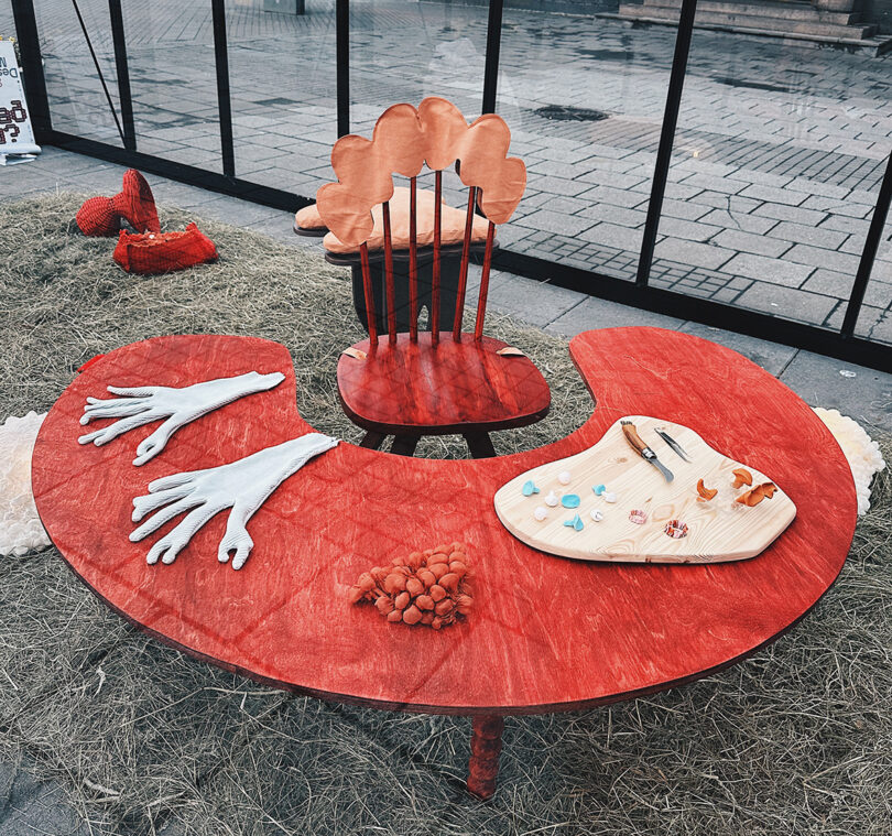 Red mushroom shaped table and chair inside a greenhouse at DesignMarch 2023 with other fungus inspired designs on the surface.