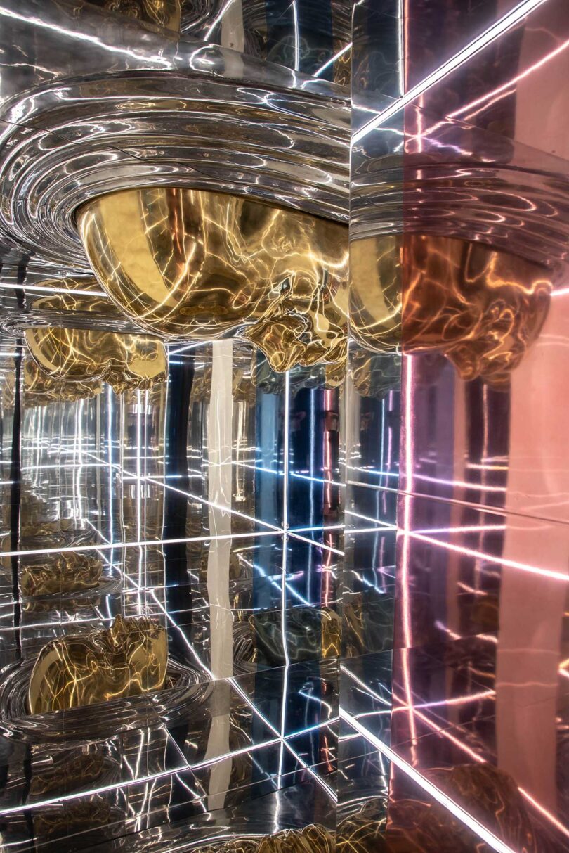 angled view of mirrored INTERNA_MENTE installation with gold faces and linear lights in white and pink