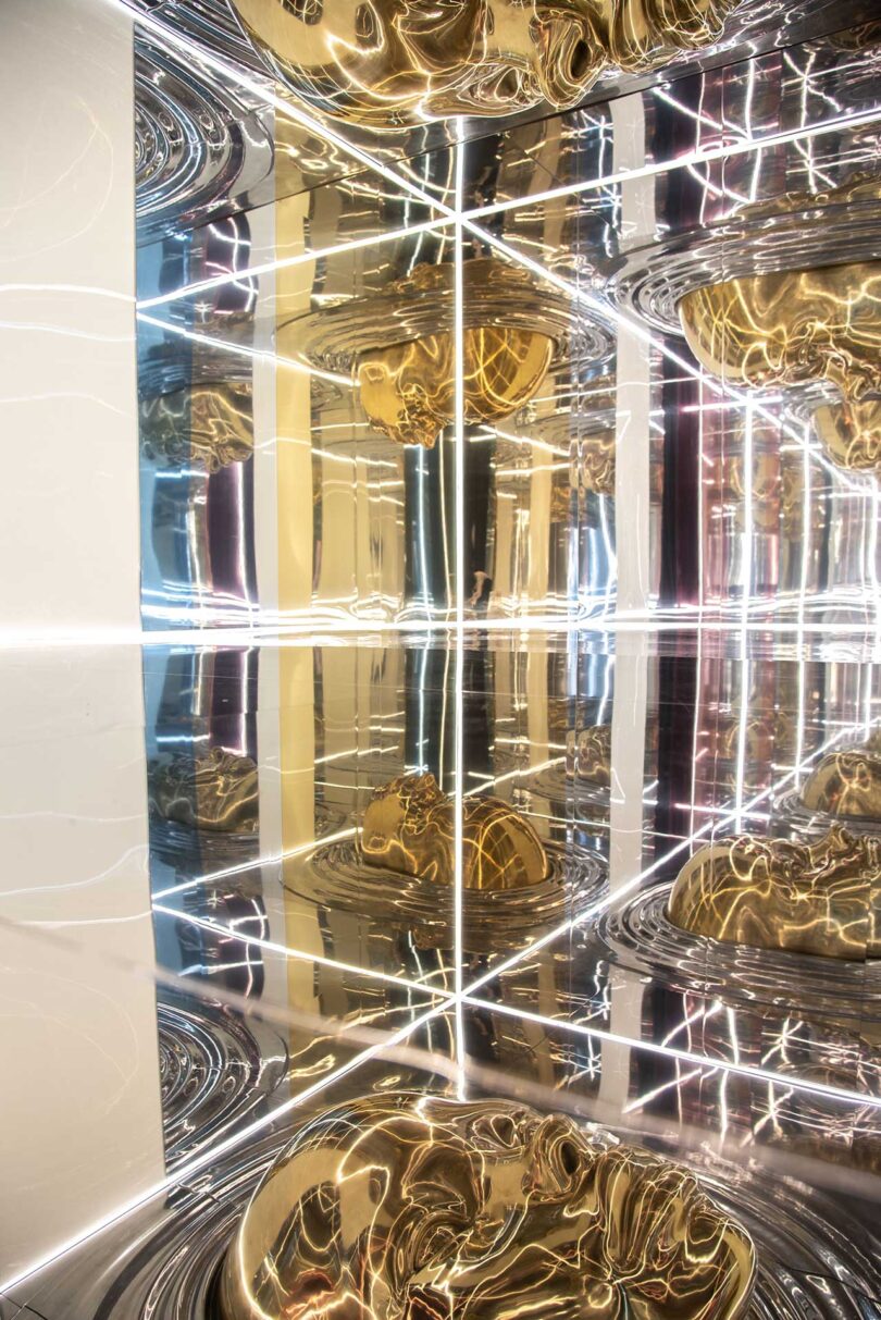 angled view of mirrored installation with gold faces and linear lights in white