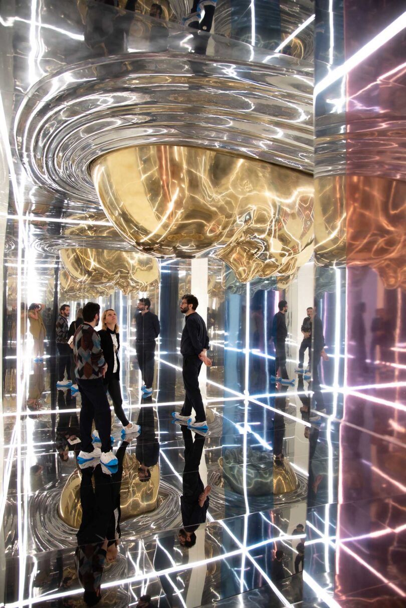 people standing around mirrored installation with gold faces and linear lights in white