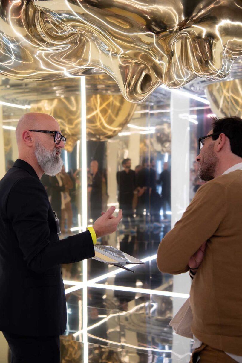 people standing around mirrored installation with gold faces and linear lights in white