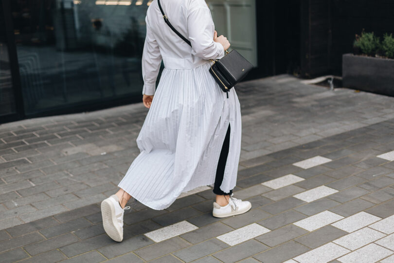 light-skinned person wearing all white carrying a black bag while walking