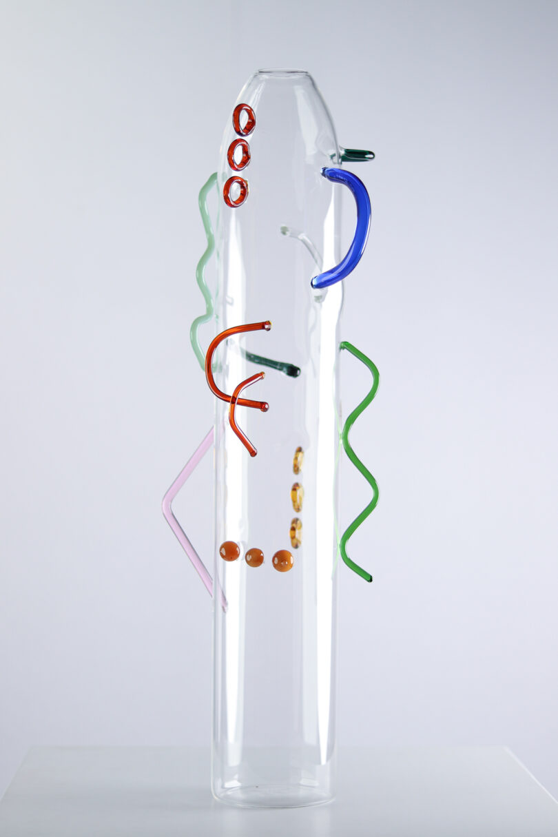 clear glass cylinder with abstract colored shapes of glass attached to the exterior