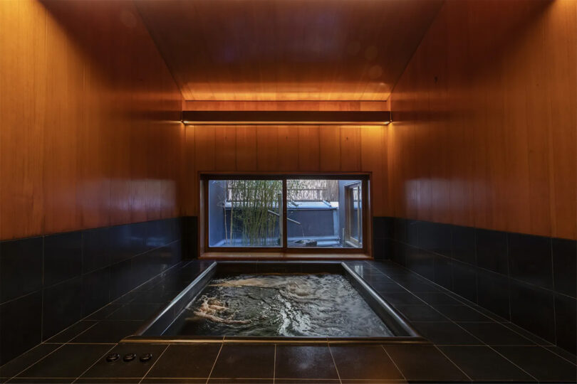 Jacuzzi tub with dark tile and wooden walls with view of bamboo courtyard
