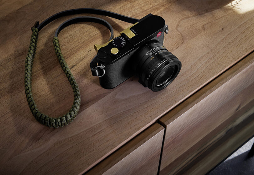 Angled view from above showing Leica Q3 camera on wood dresser drawer with braided strap attached to camera body.