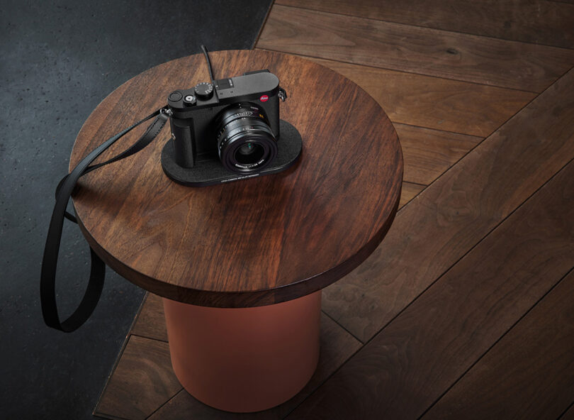 Leica Q3 wirelessly charging on Leica Wireless Charger set upon round side table.