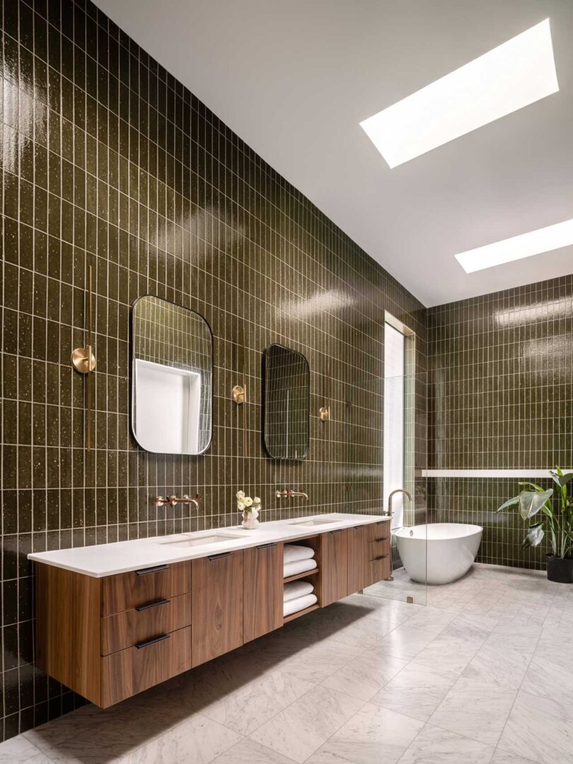 angled interior view of modern bathroom with dark green tile and wood cabinets