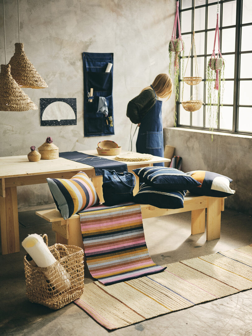 table covered in home textiles with a woman putting on a denim apron in the background
