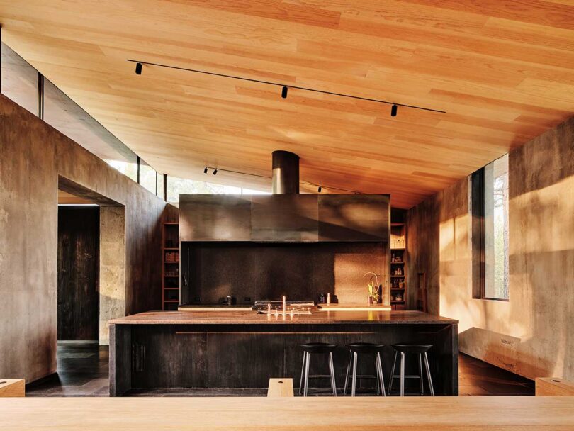 interior shot of modern home with slanted wood ceiling and blackened steel cabinets in kitchen