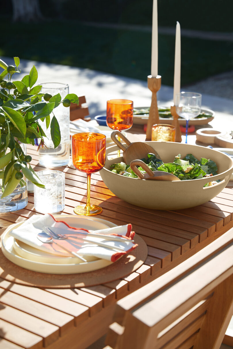 an outdoor wood table decorated with colorful kitchenwares and food