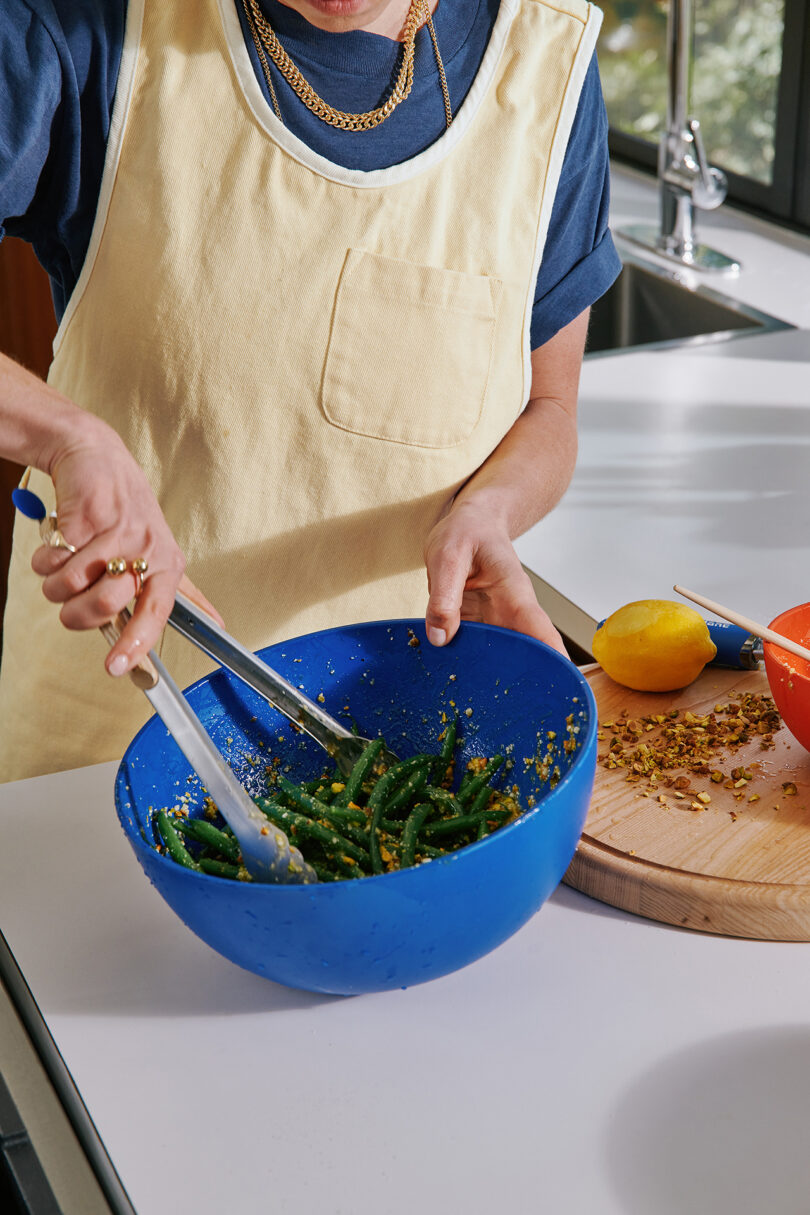 person wearing an off-white apron prepares greens in a blue bowl