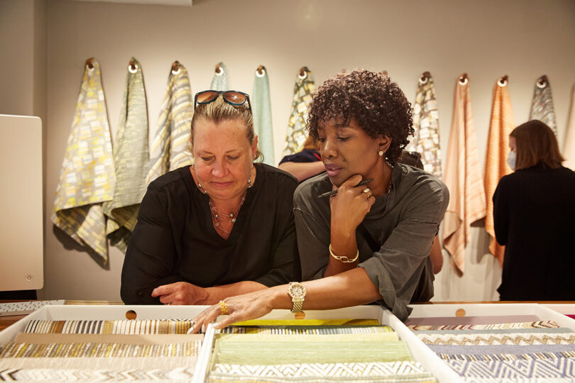 two people conversing over a tray of fabrics