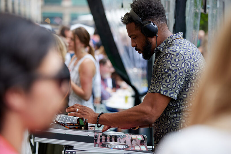a brown-skinned DJ performs at a crowded outdoor event
