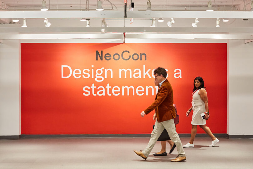 three people walk in front of a large orange sign readings NeoCon Design makes a statement
