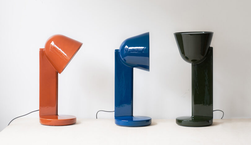 Three Ceramique lamps on table in Rust Red, Navy Blue, and Moss Green.