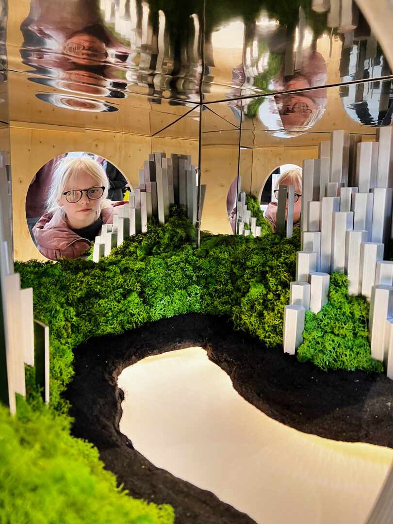 Little girl with blonde hair and glasses peering inside a box diorama of the Icelandic landscape in miniature.