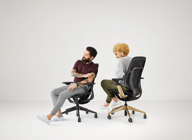 A brunette man with a beard and woman with curly blond hair seated in two Steelcase Karman chairs laughing together