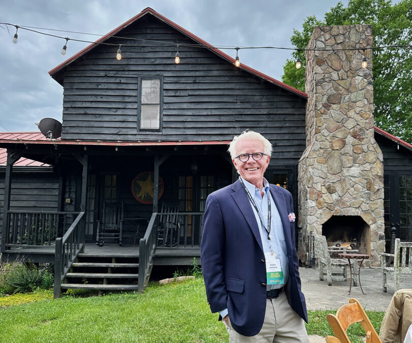 Serenbe co-founder, Steve Nygren, standing in front of an old farmhouse with stone outdoor fireplace.