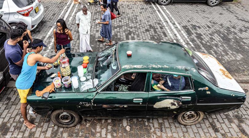 down view of old beat up green car with people serving food off hood