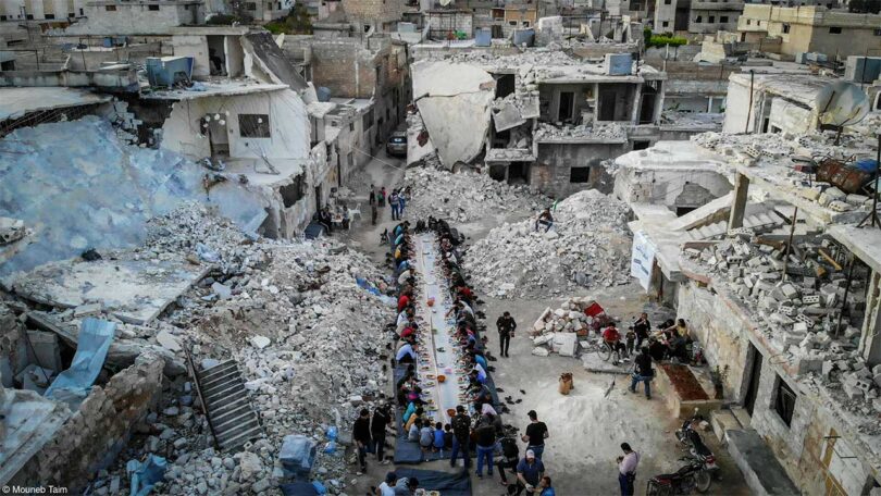 elevated view of concrete ruins of city in Syria with people around table eating