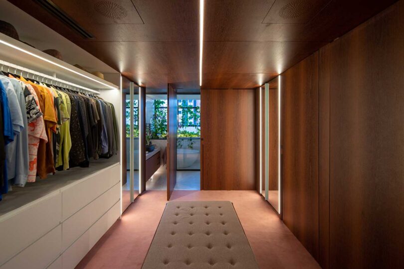 view of long modern closet with dark wood doors with view into bathroom
