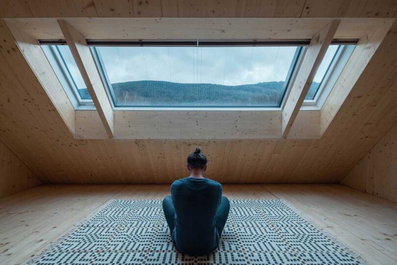 person meditating in center of modern room with slanted wall with windows