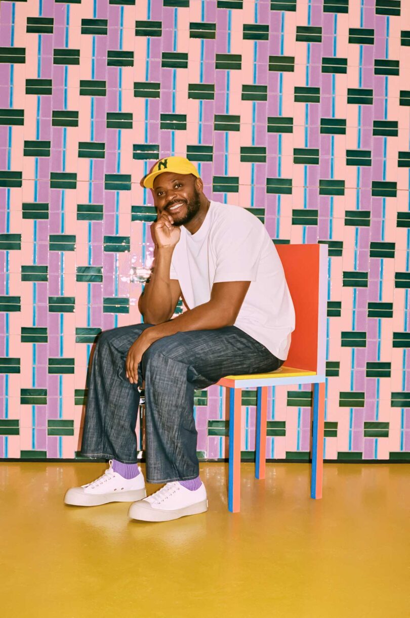 Yinka Ilori sitting in colorful chair in front of colorful tile wall