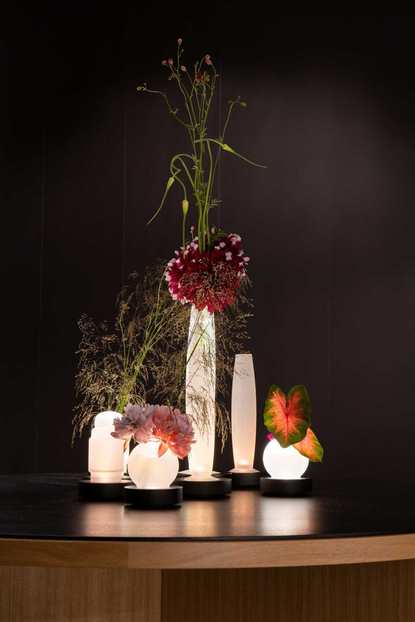 five illuminated vases of different shapes and sizes with flowers
