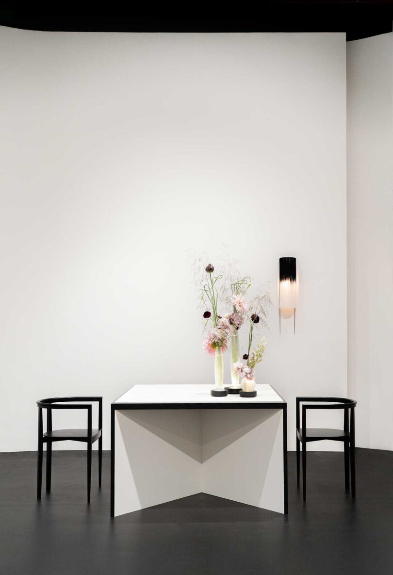 square white dining table with two black armchairs and a vase of florals
