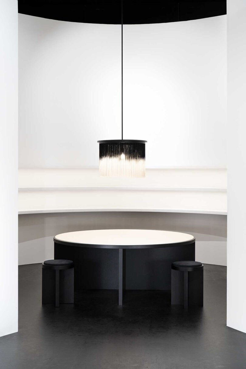 round black and white dining table with coordinating black stools and a black pendant light overhead