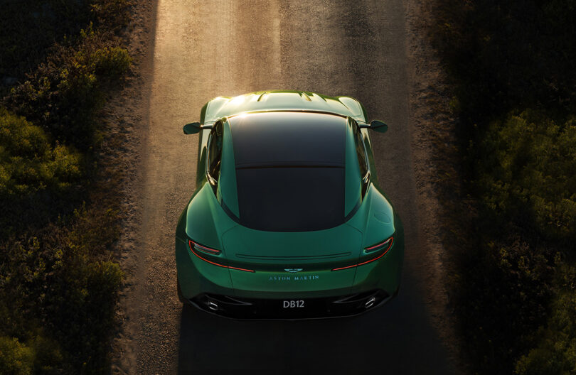 Back overhead view of Iridescent Green Aston Martin DB12 riding into the sunset.
