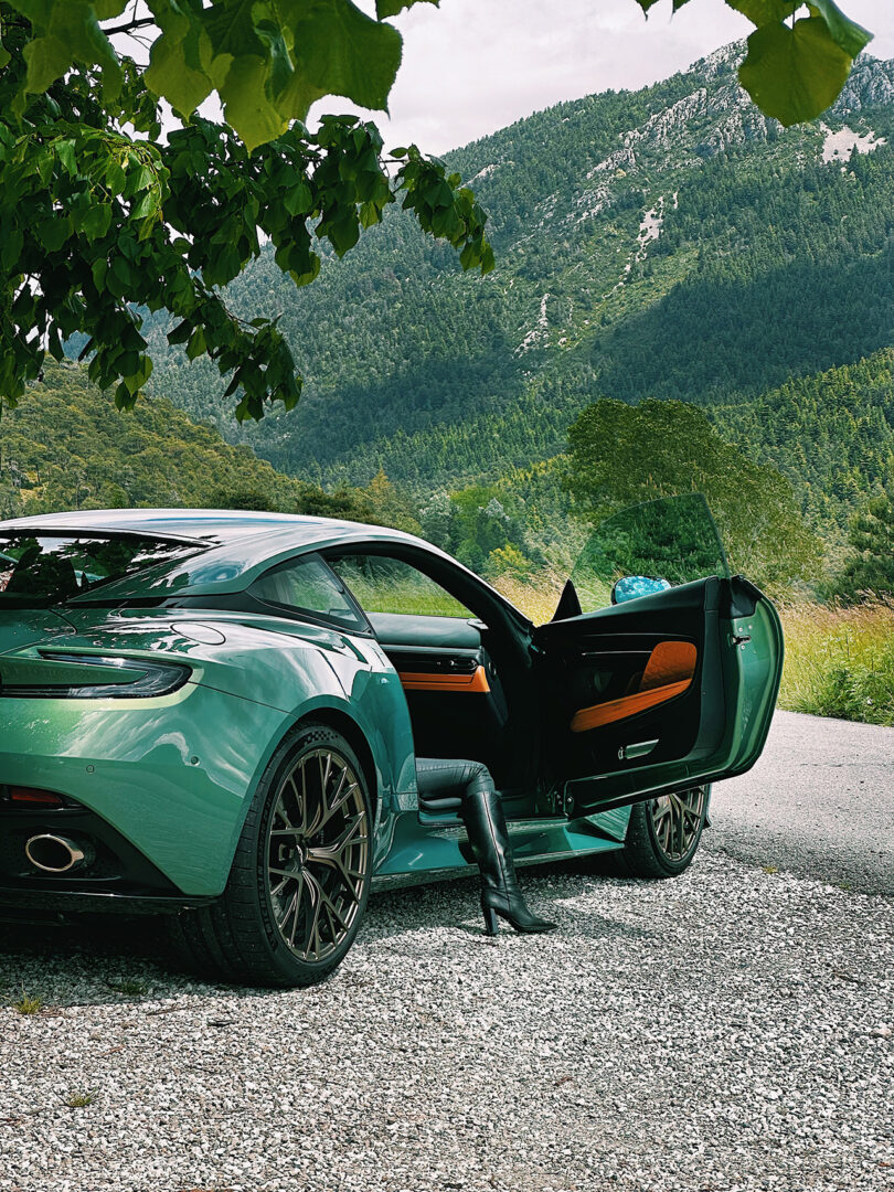 Woman with boot covered leg sticking out from driver's side of the Aston Martin DB12 in Iridescent Green.
