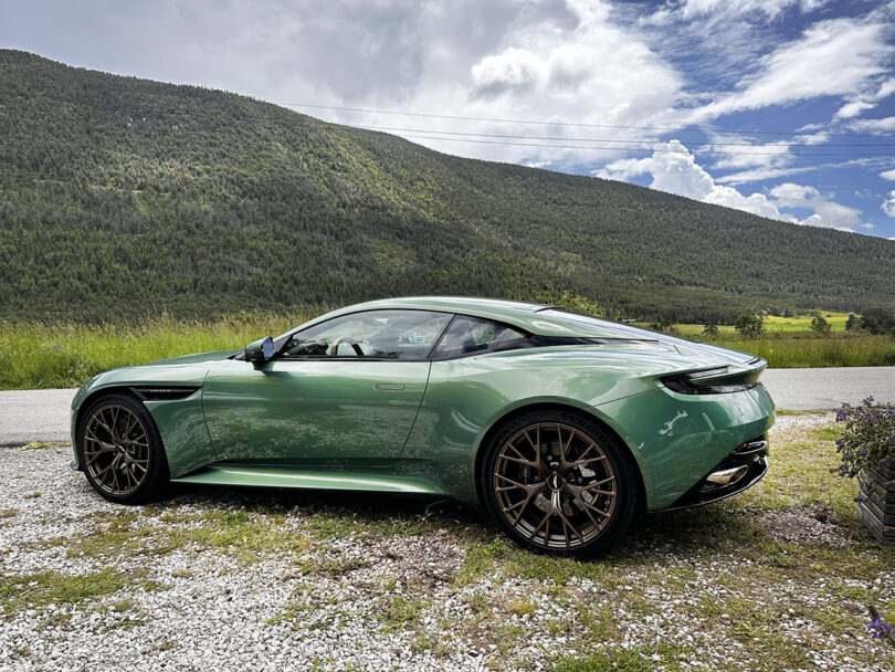 Aston Martin DB12 in Iridescent Green parked along gravel roadside in French countryside.