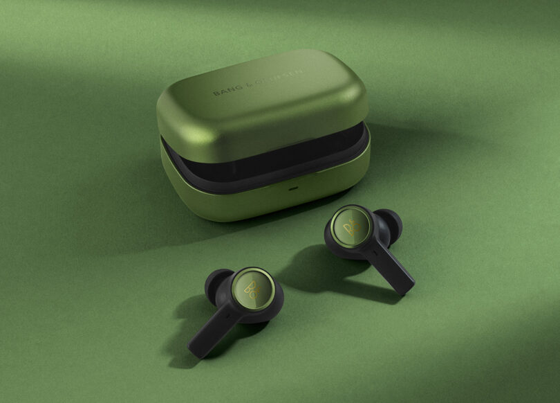 Forest Green Beoplay EX earphones with charging case set on green background and surface.