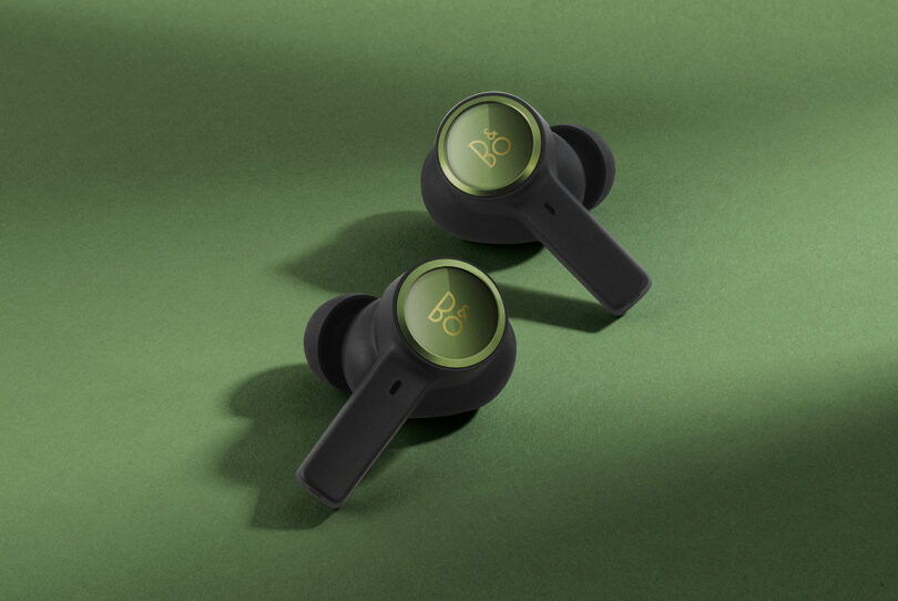 Detail of two Forest Green Beoplay EX earbuds set on green background and surface.
