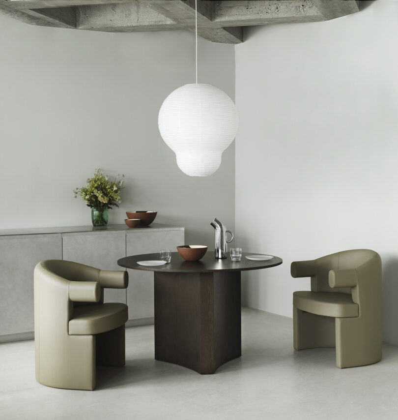 two dark beige dining armchairs at a dark round table in a styled space