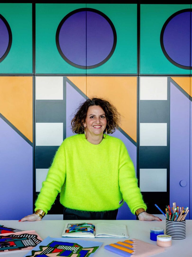 Camille Walala in bright neon yellow sweater in front of geometric cabinets