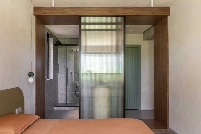 side view of modern bedroom with peach bedding and sliding glass doors opening up to the bathroom
