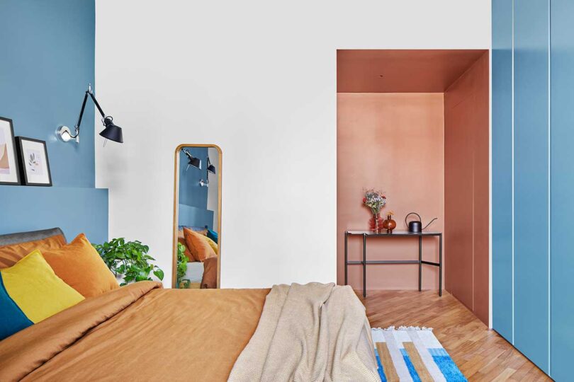 نمای جانبی اتاق خواب مدرن که از روی تخت با ملافه های هلویی و لهجه های آبی به نظر می رسد