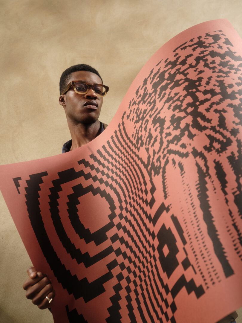 brown-skinned man with glasses holds up a black and orange screen print