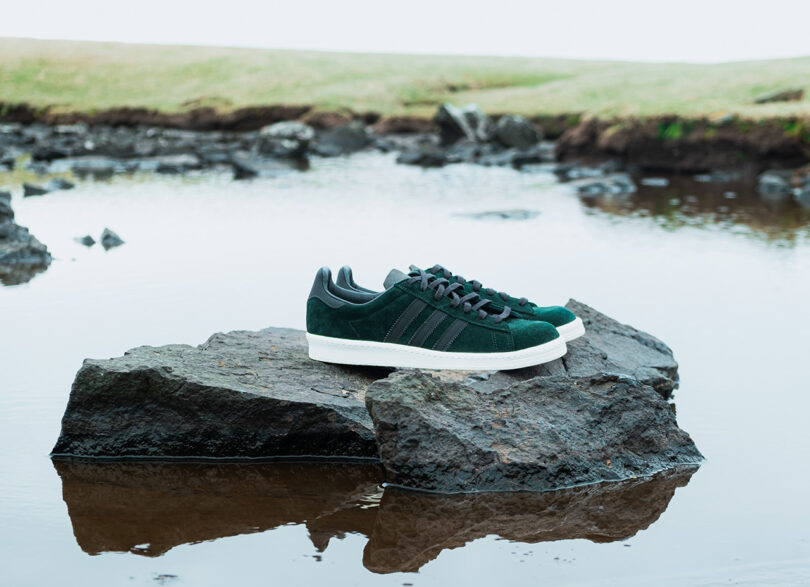 Dark green Norse Projects x Adidas Campus 80s in dark green set on rocks jutting from water in the Faroe Islands.