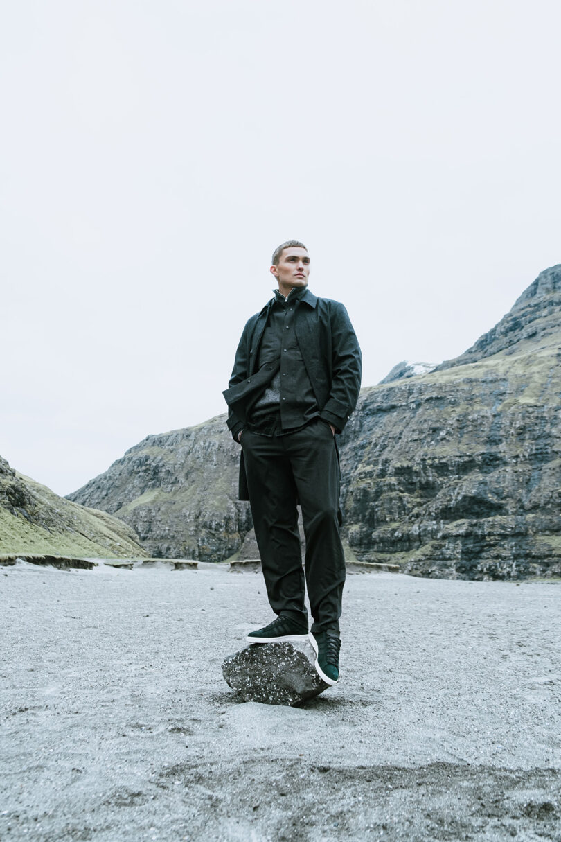 Young man standing balanced upon a rock set on the sandy beach of the Faroe Islands.