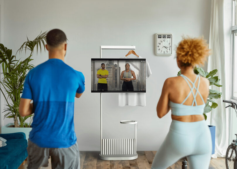 two people standing facing away looking at TV mounted on white stand