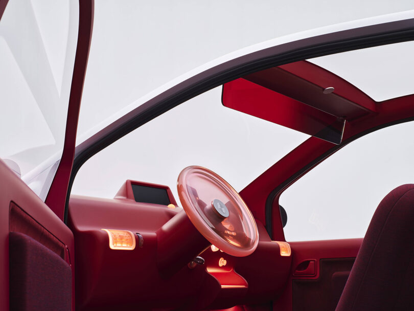 Driver side door opened to reveal the all red interior of the 30th anniversary Renault Twingo, centered by an transparent red steering wheel.