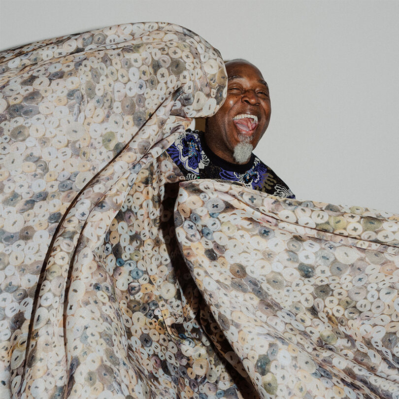 brown-skinned man with a large piece of printed fabric and a big smile on his face