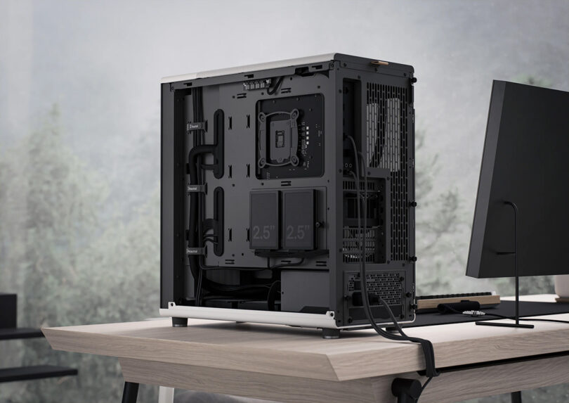 Black PC tower case with on left side of a wood desk and a flat simulated monitor seen from rear with side panels open, revealing two 2.5-inch solid state drives and speaker.